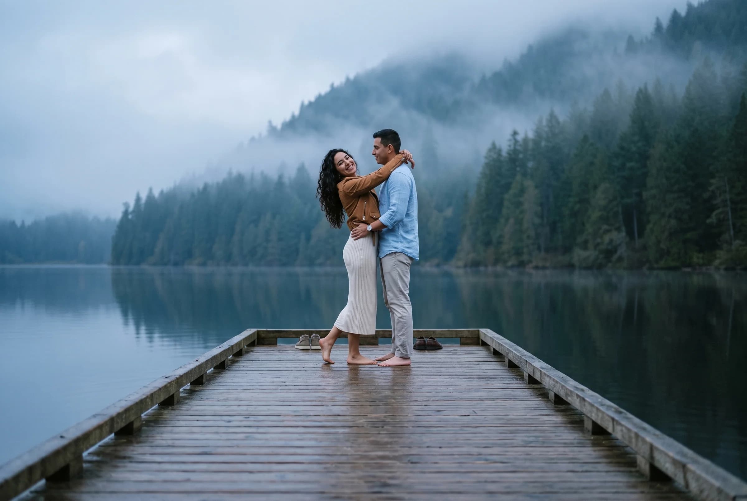 Couple on the floating dock at Buntzen Lake in early morning mist with forested ridges behind