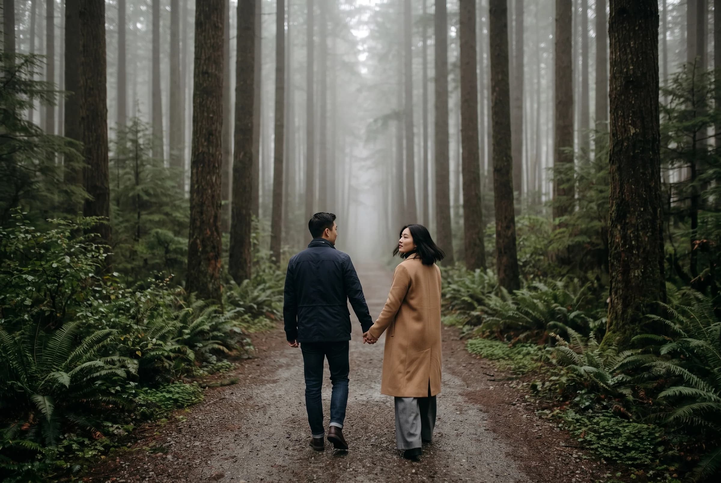 Couple walking hand in hand away down a wide forest trail in heavy fog at Pacific Spirit Regional Park
