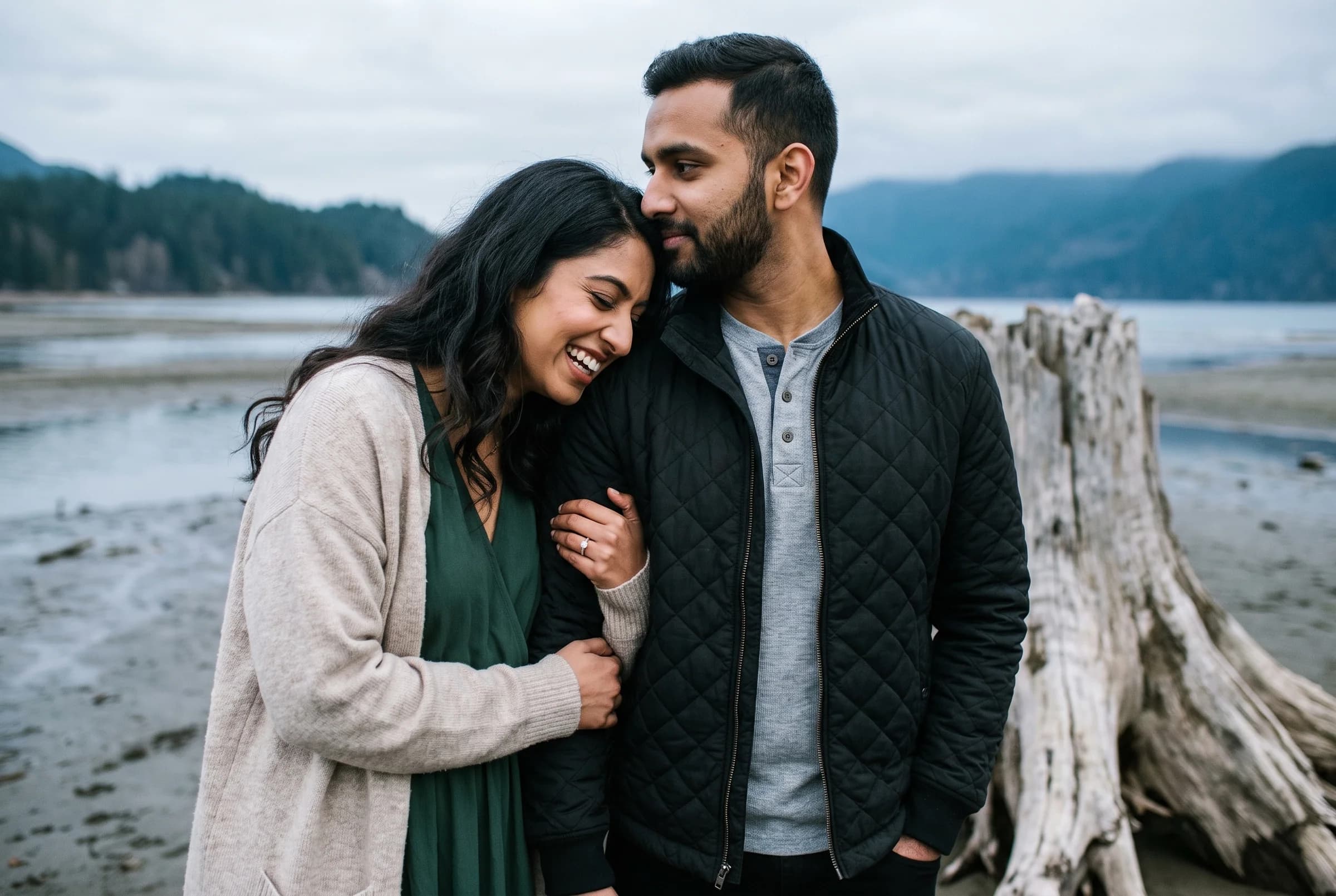 Couple standing close together among bleached tree stumps on the grey shoreline of Stave Lake